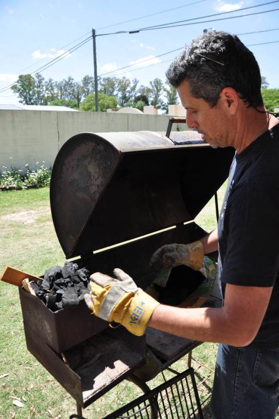Che Toba inicia o asado preparando o carvão e o algarrobo para queimar, em Villa Nueva, na Argentina